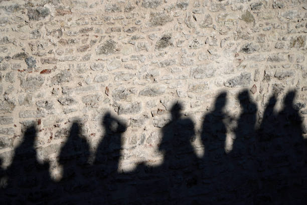 Creative shadow of four people with raised hands on a wall, concept of friendship, unity, joy, teamwork, and freedom