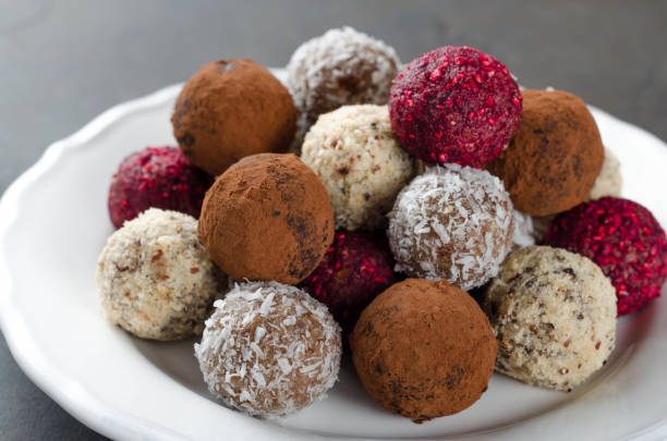 istock Homemade vegan chocolate candies with dried raspberry, grated coconut, nuts, cocoa on a white plate and dark stone background. Selective focus 868697572