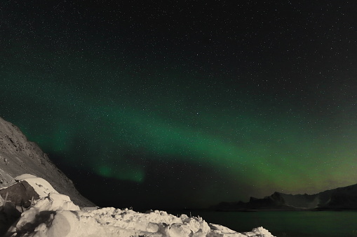 Green lights-aurora borealis illuminate from the N.mounts Ytresandheia-Roren to the E.at Yttresand village on Sandbotnen bay-N.Flakstadoya island on a cold quiet night. Lofoten-Nordland fylke-Norway.