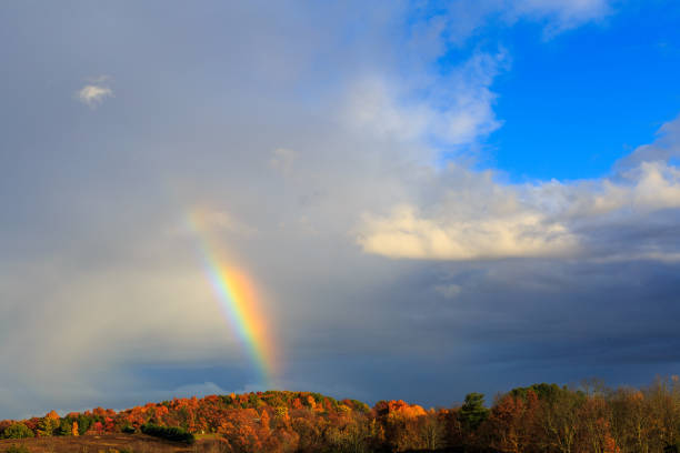 Rainbow over Berkshires and Hudson Valley NY during fall time and rain storm. Sky gray and blue. Leaves orange and yellow.