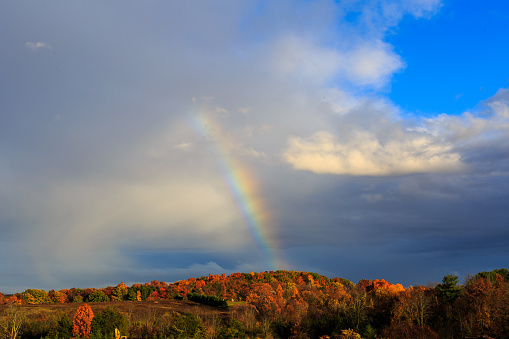 Rainbow over Berkshires and Hudson Valley NY during fall time and rain storm. Sky gray and blue. Leaves orange and yellow.