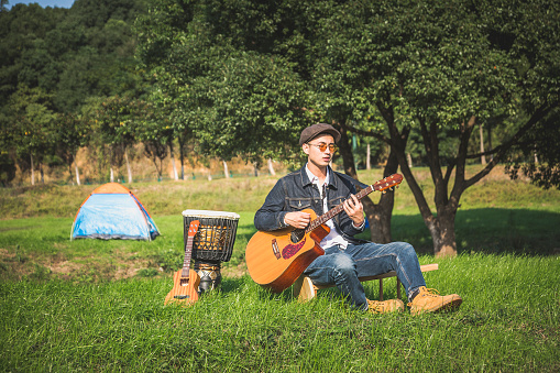 young man playing musical instrument on lawn during camping.