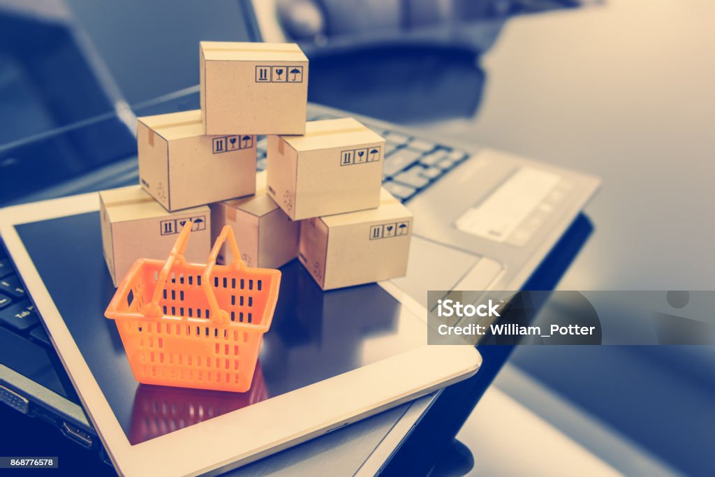 Mini cesta naranja en un dispositivo inteligente y un ordenador portátil con las cajas. Concepto de compras a que el cliente puede comprar o adquirir bienes o productos de los sitios web en todo el mundo a través de internet por un par de clics. - Foto de stock de Venta al por menor libre de derechos