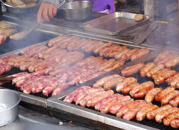An outdoor vendor roasts fresh pork sausages on a grill