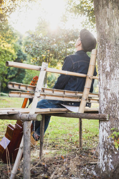 istock young pensive man sitting on wooden bench with guitar 868782772