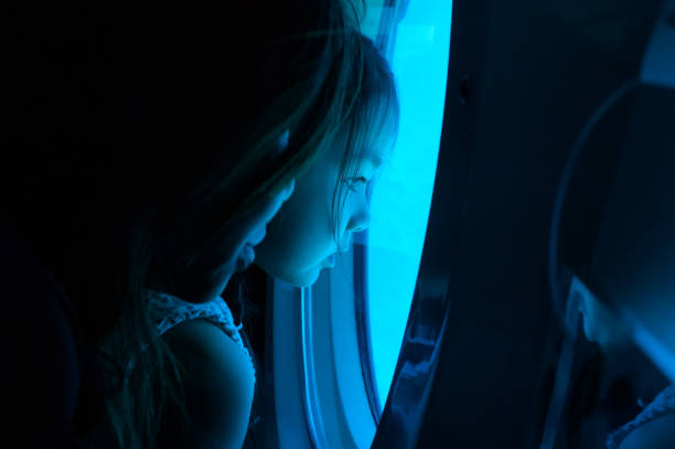 Little girl looking through window in submarine stock photo