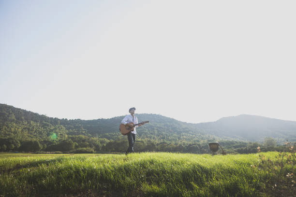 asian male musician playing guitar against sky.
