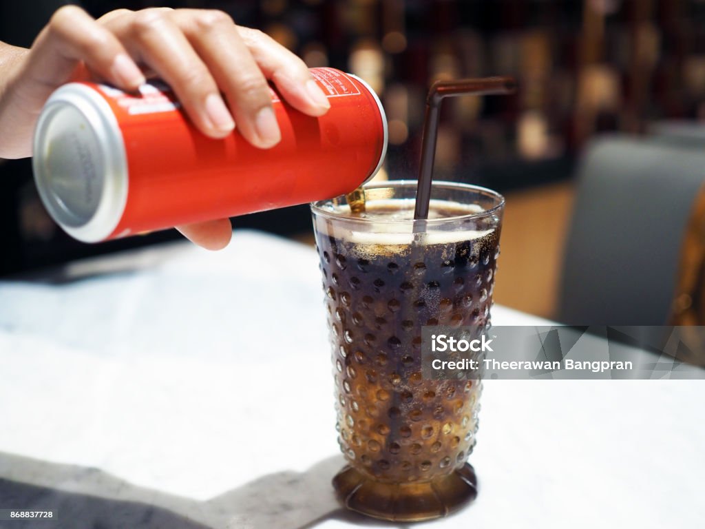 Pouring cola over ice cube in clear glass with straw. Pouring cola over ice cube in clear glass with straw. Selective focus Can Stock Photo