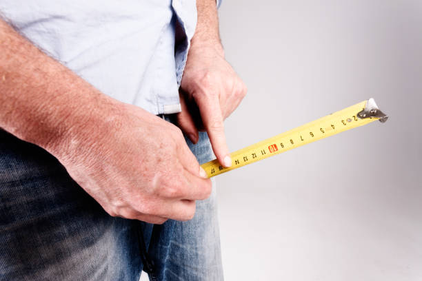 Male hands hold measuring tape to crotch An unrecognizable man's hands hold a tape measure to the crotch of his jeans, checking size or growth with his forefinger. penis photos stock pictures, royalty-free photos & images