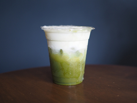 A plastic glass of iced green tea latte with layer of fresh foam milk on table background, selective focus.