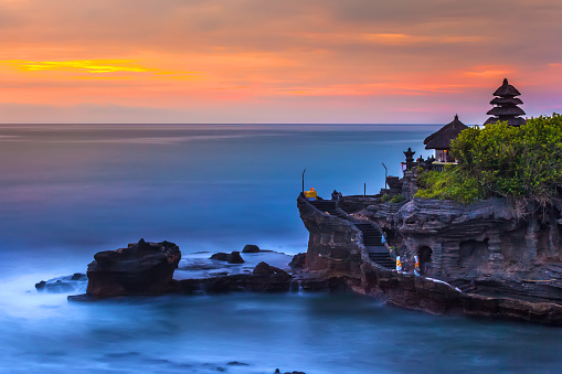 The Pilgrimage Temple of Pura Tanah Lot at sunset, island with an Indonesian shrine on the ocean, long exposure, copy space for text.