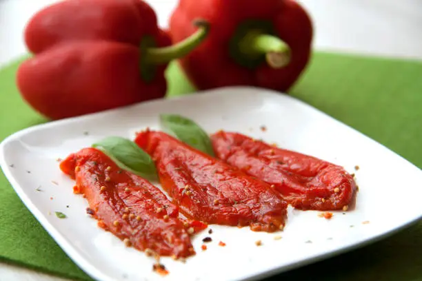 Three skinless slices of baked red bell pepper on a white plate.