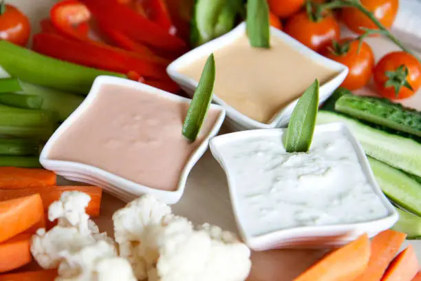 Variety of vegetables on a big plate and three different dressings.