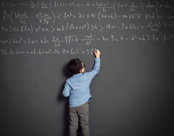 Cute child in front of huge blackboard. He knows answer. He writing formula.