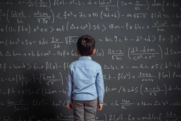 Cute child in front of huge blackboard. He knows answer.