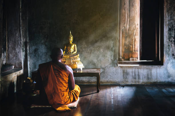 A monk is worshiping and meditating in front of the golden Buddha as part of Buddhist activities.Focus on the Buddha stock photo