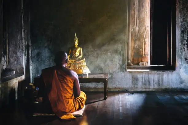 Photo of A monk is worshiping and meditating in front of the golden Buddha as part of Buddhist activities.Focus on the Buddha