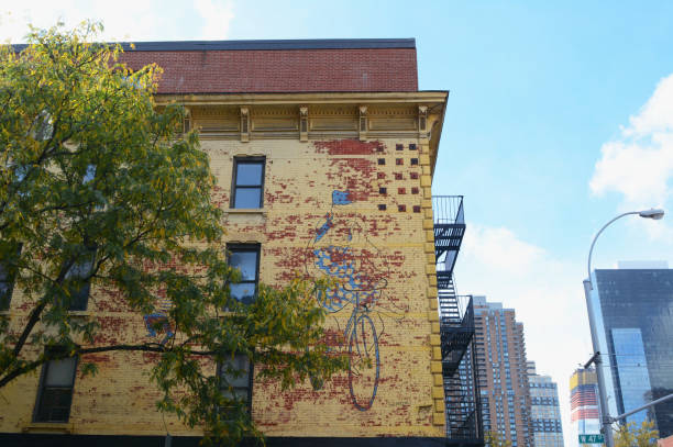 NEW YORK - OCTOBER 23, 2017: Wall of Kiehl's building on the corner of West 37th Street and 9th Avenue, with peeling yellow paint and weathered mural artwork. Honey locust tree in foreground, starting to show fall color.