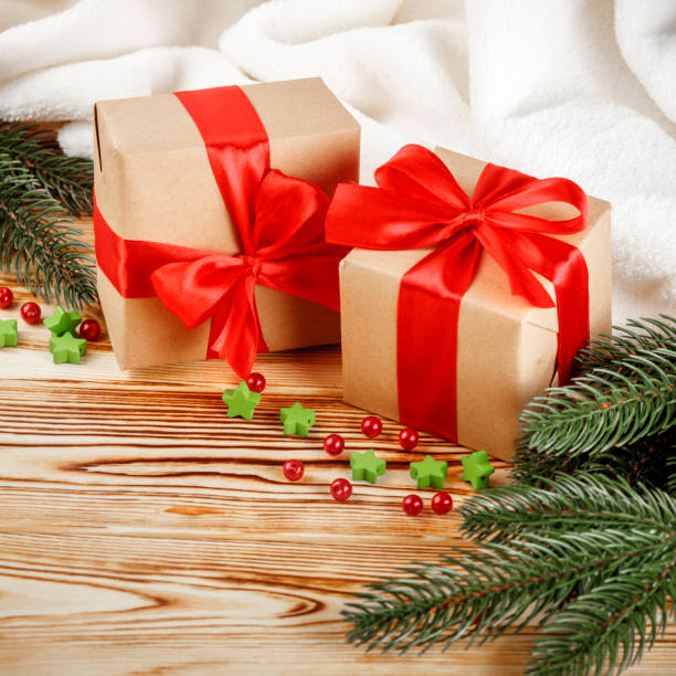 istock Craft gift boxes with red ribbon and bow, green Christmas tree, decorations, white plaid on wooden background. Xmas and New Year congratulation card, banner, flyer. 868895876
