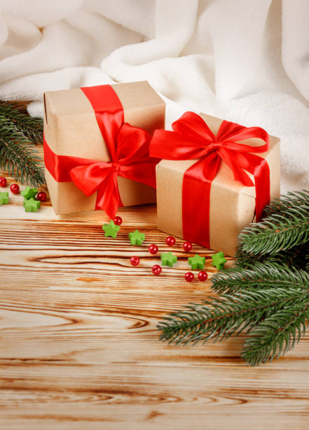 istock Craft gift boxes with red ribbon and bow, green Christmas tree, decorations, white plaid on wooden background. Xmas and New Year congratulation card, banner, flyer. 868895880