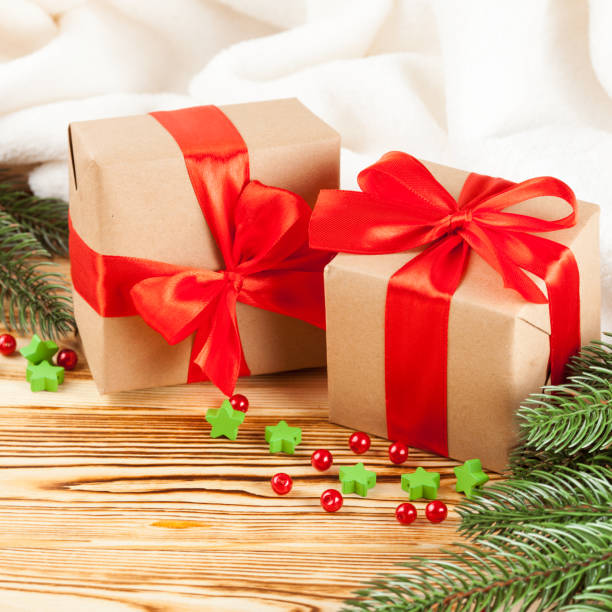 istock Craft gift boxes with red ribbon and bow, green Christmas tree, decorations, white plaid on wooden background. Xmas and New Year congratulation card, banner, flyer. 868895958