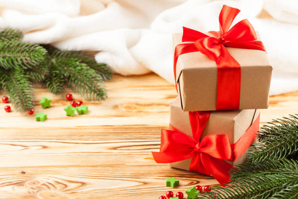 istock Craft gift boxes with red ribbon and bow, green Christmas tree, decorations, white plaid on wooden background. Xmas and New Year congratulation card, banner, flyer. 868895960