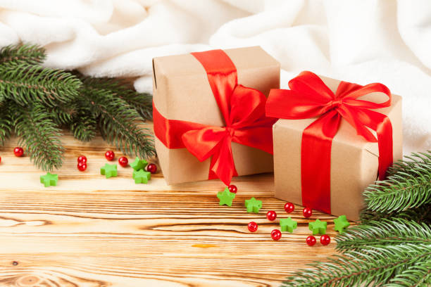 istock Craft gift boxes with red ribbon and bow, green Christmas tree, decorations, white plaid on wooden background. Xmas and New Year congratulation card, banner, flyer. 868895964