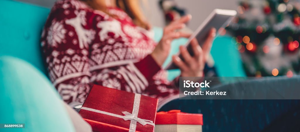 Christmas presents on the sofa Christmas presents laying down on the sofa and women using tablet to shopping online is visible in the background Christmas Stock Photo