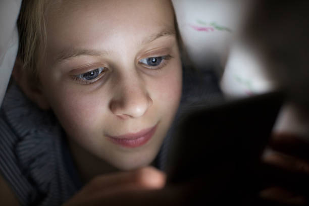 istock Girl Using Mobile Phone Hiding Under Duvet In Bed At Night 868899704