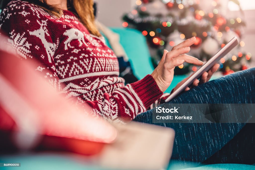 Women using tablet during christmas Women sitting on the blue sofa by the christmas tree and using tablet Christmas Stock Photo