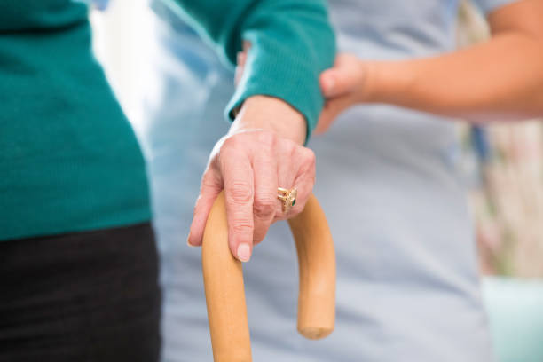 istock Senior Woman's Hands On Walking Stick With Care Worker In Background 868900594