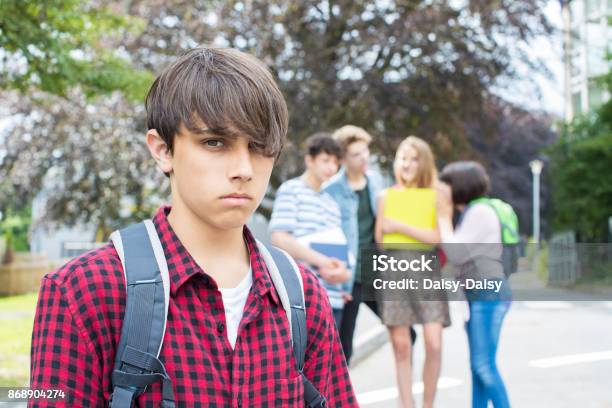 Unhappy Boy Being Gossiped About By School Friends Stock Photo - Download Image Now - Bullying, Education, Teenage Boys
