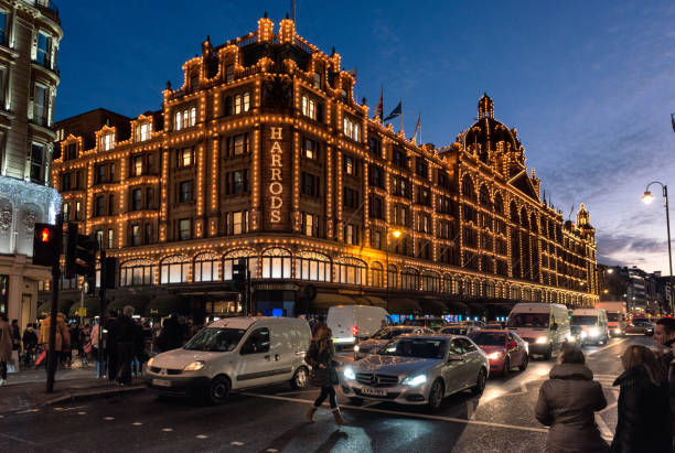 Harrods of London at dusk London, UK - Pedestrians and traffic on the street in front of the illuminated facade of Harrods Department Store in Kensington. harrods photos stock pictures, royalty-free photos & images