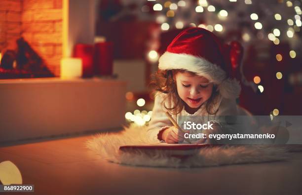 Muchacha Del Niño Escribiendo La Carta A Casa Santa Cerca De Árbol De Navidad Foto de stock y más banco de imágenes de Navidad