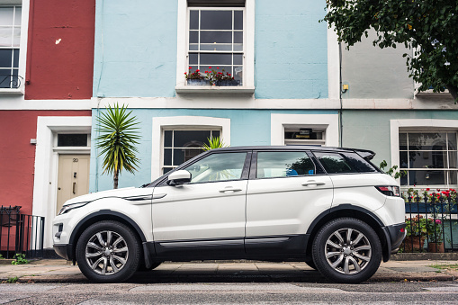 London, UK - Side view of a white Range Rover Evoque, parked on a street of pastel coloured homes.