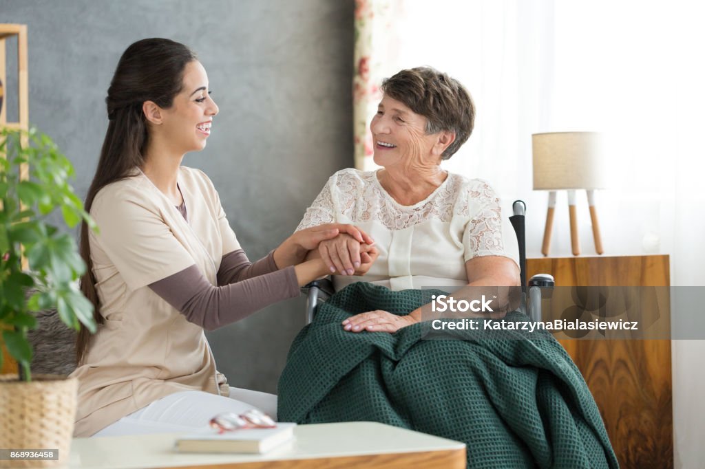 Smiling woman and happy grandmother Smiling woman taking care about happy grandmother in wheelchair with green blanket on legs Parkinson's Disease Stock Photo