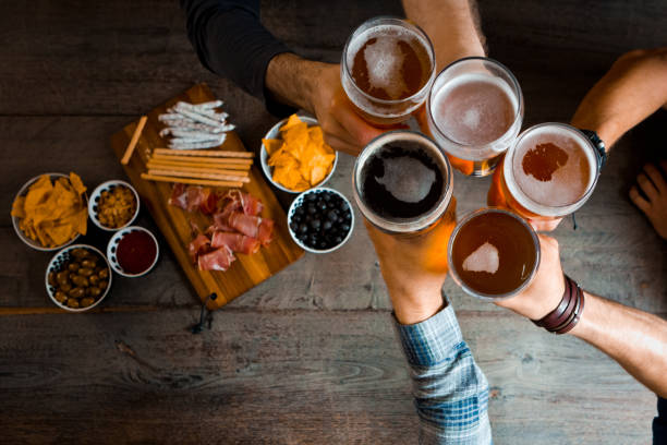 Draufsicht von Freunden, die mit Biergläsern in der Kneipe anstoßen. Unkenntliche Menschen. Hochwinkelansicht der Tabelle.