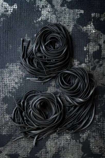 Detox charcoal or black squid ink fettuccine on grey background.