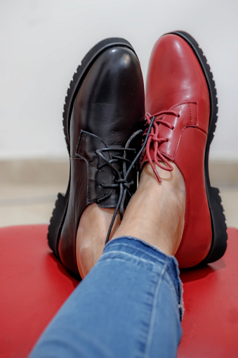 Part of the female legs in jeans are shod in different color shoes on a red stool