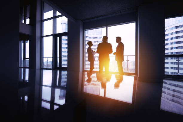 istock Group businessmen silhouettes three office big window concept 868959534