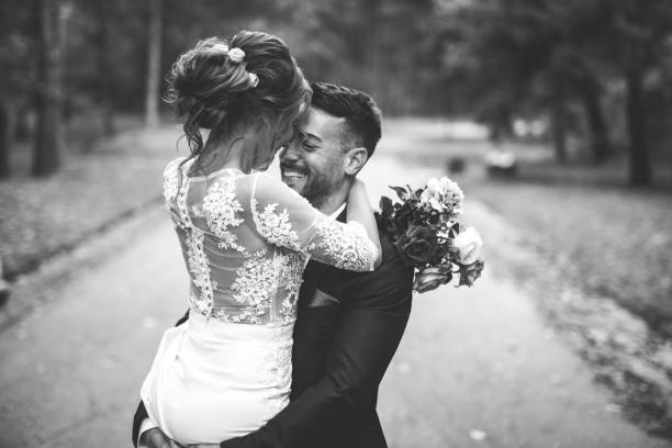 Happy bride and groom in black and white Groom is holding a bride in his arms and spinning her around spinning in the park on their wedding day wedding dress photos stock pictures, royalty-free photos & images
