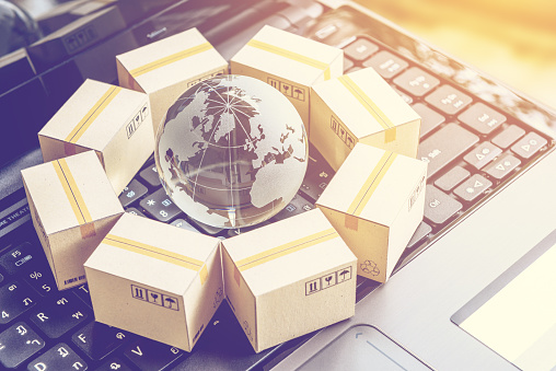 International freight or shipping service for online shopping or ecommerce concept : Paper boxes or carton put in circle around a clear crystal globe with world map on a computer notebook keyboard.