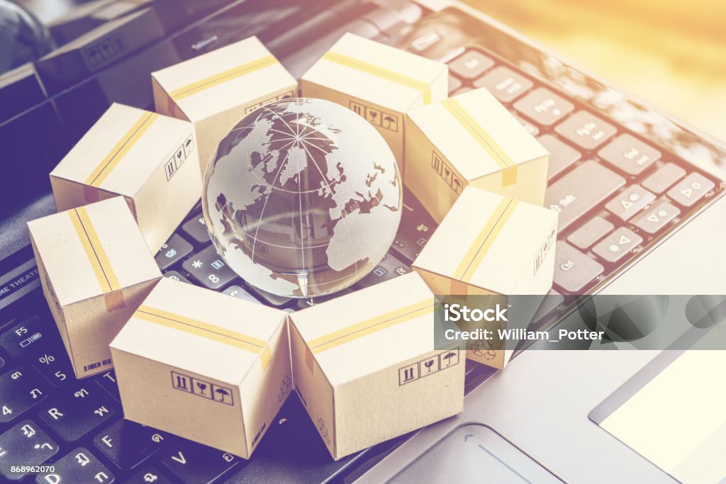 International freight or shipping service for online shopping or ecommerce concept : Paper boxes or carton put in circle around a clear crystal globe with world map on a computer notebook keyboard. Global Stock Photo