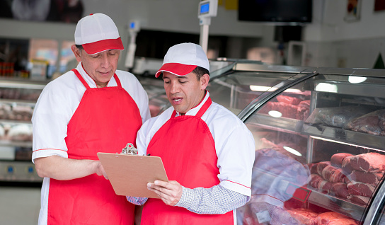 Portrait of two men working at the butchery and looking at the inventory on a clipboard