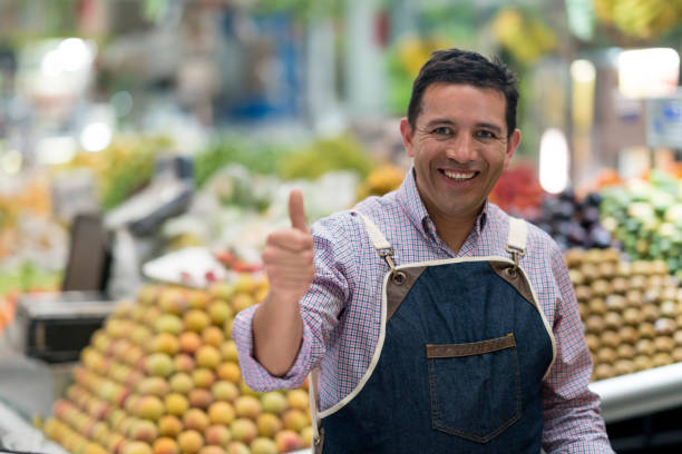 Portrait of a happy man with thumbs up working at a supermarket and looking at the camera smiling