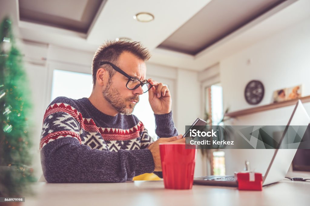 Man using smart phone at home Man wearing blue sweater and eyeglasses using smart phone at home during christmas holidays Winter Stock Photo