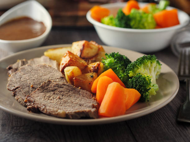 British Roasted beef dinner Traditional British Dish roasted beef with roasted potatoes and steamed carrot and broccoli,service with home made gravy carving set stock pictures, royalty-free photos & images