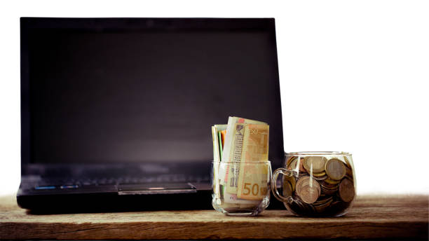 Business and Finance concept, various kinds of currency coin and selective on fifty euro note put in clear glass and laptop on the beautiful textured wooden board.Image with dual-iso and stacked focus, macro photography.Used for money saving or income from engineering work concepto de finanzas y negocios, de diversos tipos de moneda monedas y selectiva en el billete de cincuenta euros en vidrio claro y el ordenador portátil en el tablero de madera con textura hermosa. imagen con iso dual y focus apilada, fotografía macro. utilizado para ahorrar dinero o ingresos para