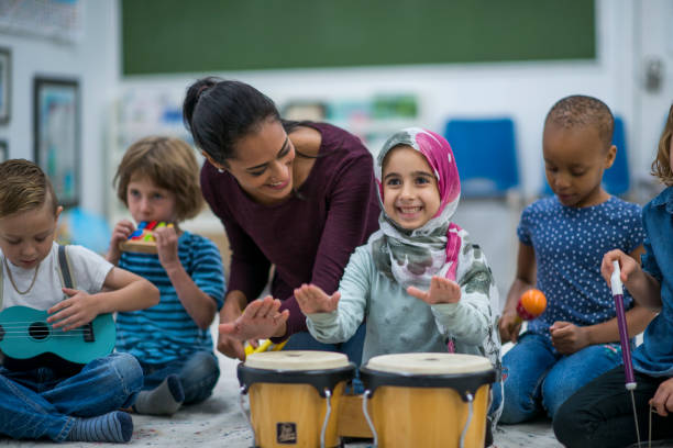 Little Muslim girl enjoy music class at school with her friends. Little Muslim girl wearing a hijab is enjoying playing music with her friends and teacher at school.  She is happy and playing the drums. religious dress stock pictures, royalty-free photos & images