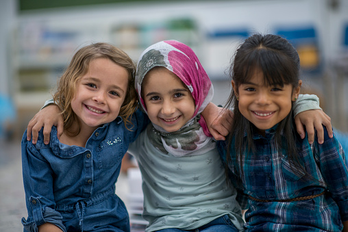 Little Muslim girl wearing a hijab is enjoying the day at school with her friends.